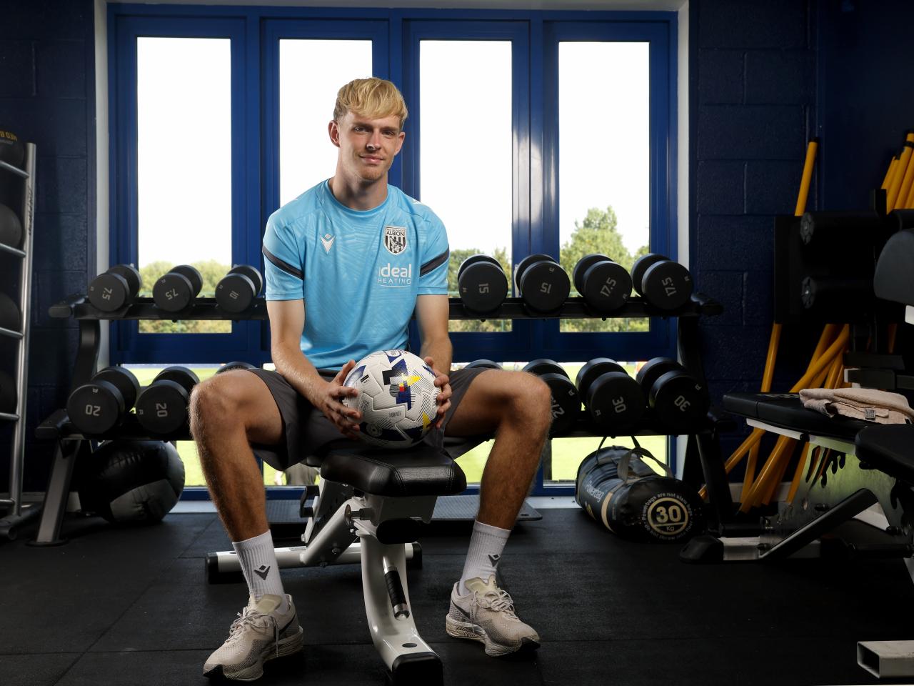 Toby Collyer sat on a bench in the gym smiling at the camera holding a ball