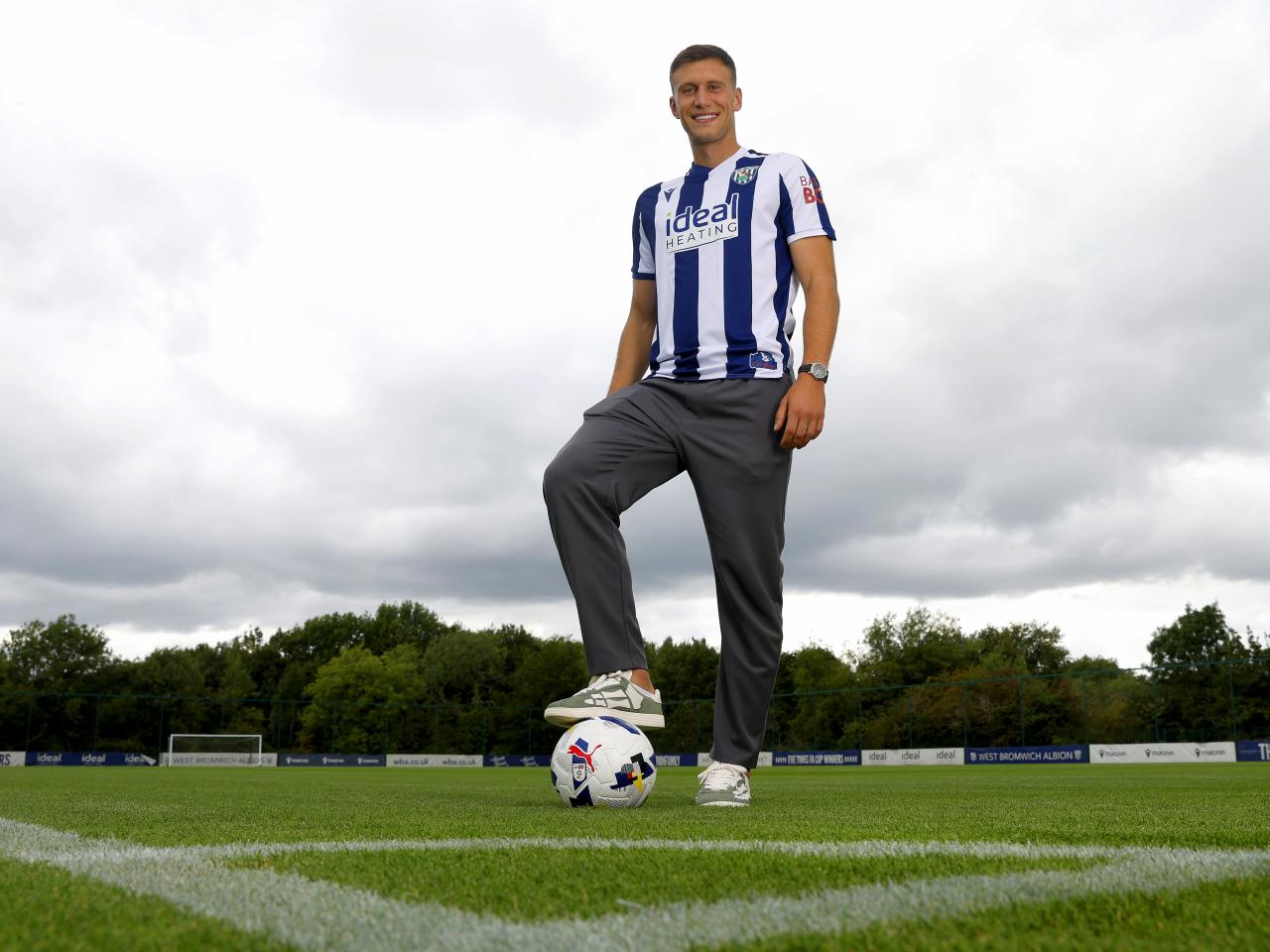 Krystian Bielik smiling at the camera while stood in the home shirt with one foot on the ball