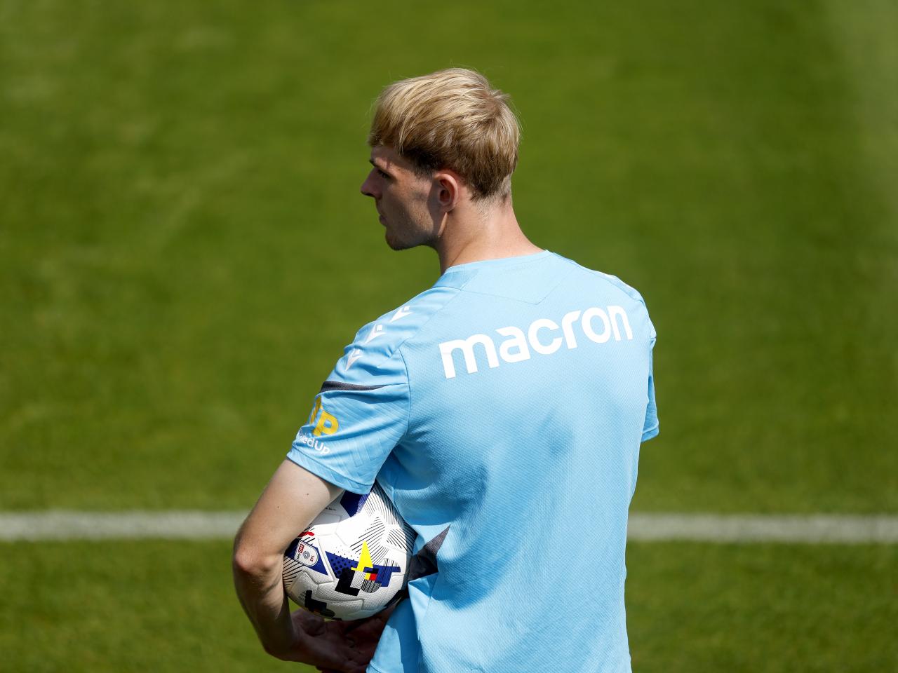 Toby Collyer holding a ball watching training with his back to the camera 
