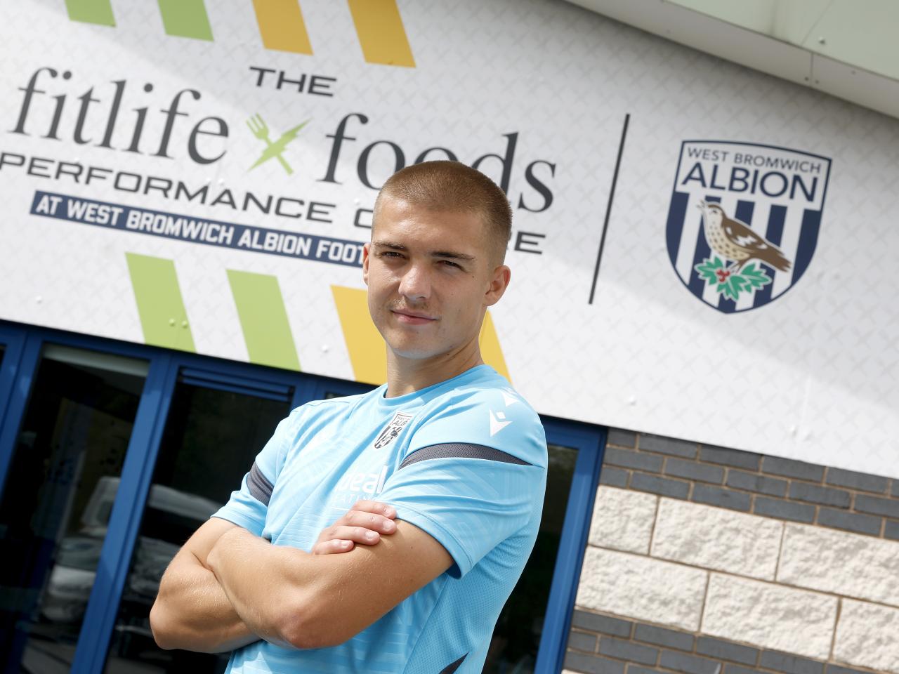 Alfie Gilchrist outside the front of the training ground with his arms folded looking at the camera 