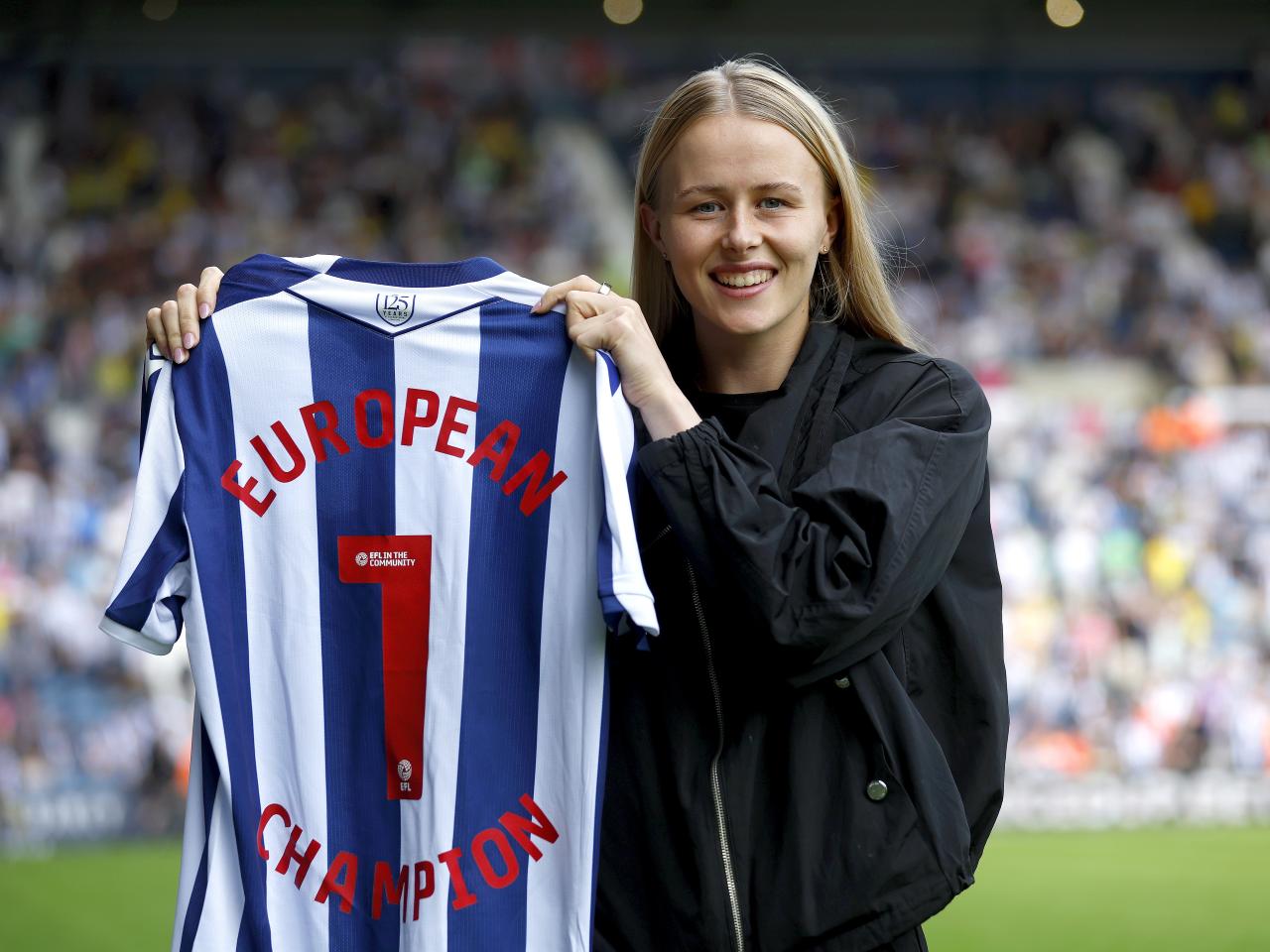 Hannah Hampton posing for a photo with an Albion shirt with her name and a No.1