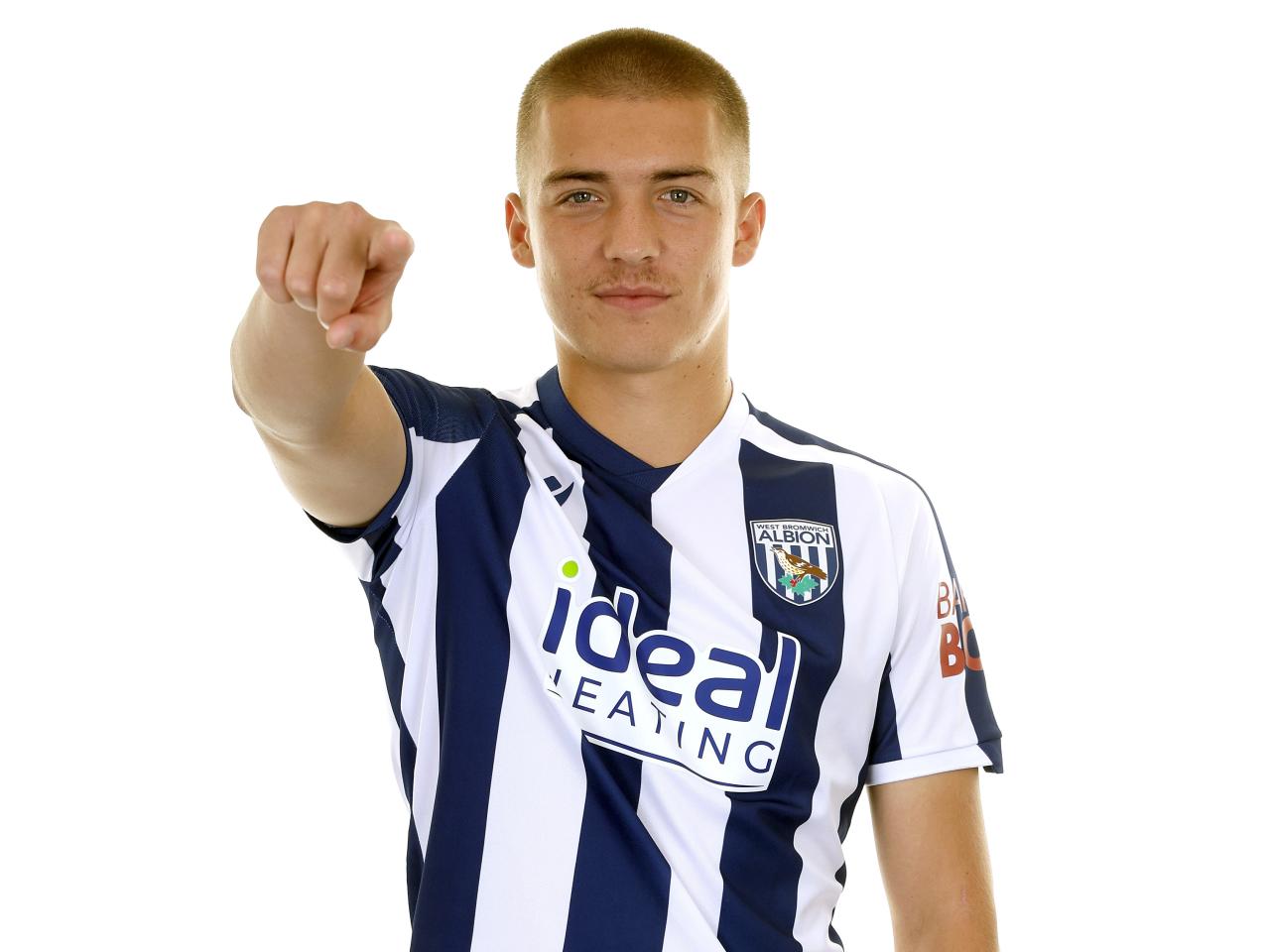 Alfie Gilchrist smiling and pointing at the camera while stood in a home shirt