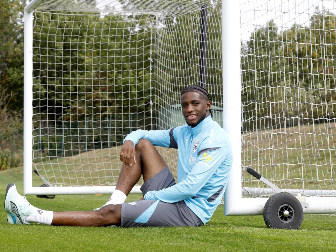 Samuel Iling-Junior smiling at the camera while sat up against a goal post on the training pitch