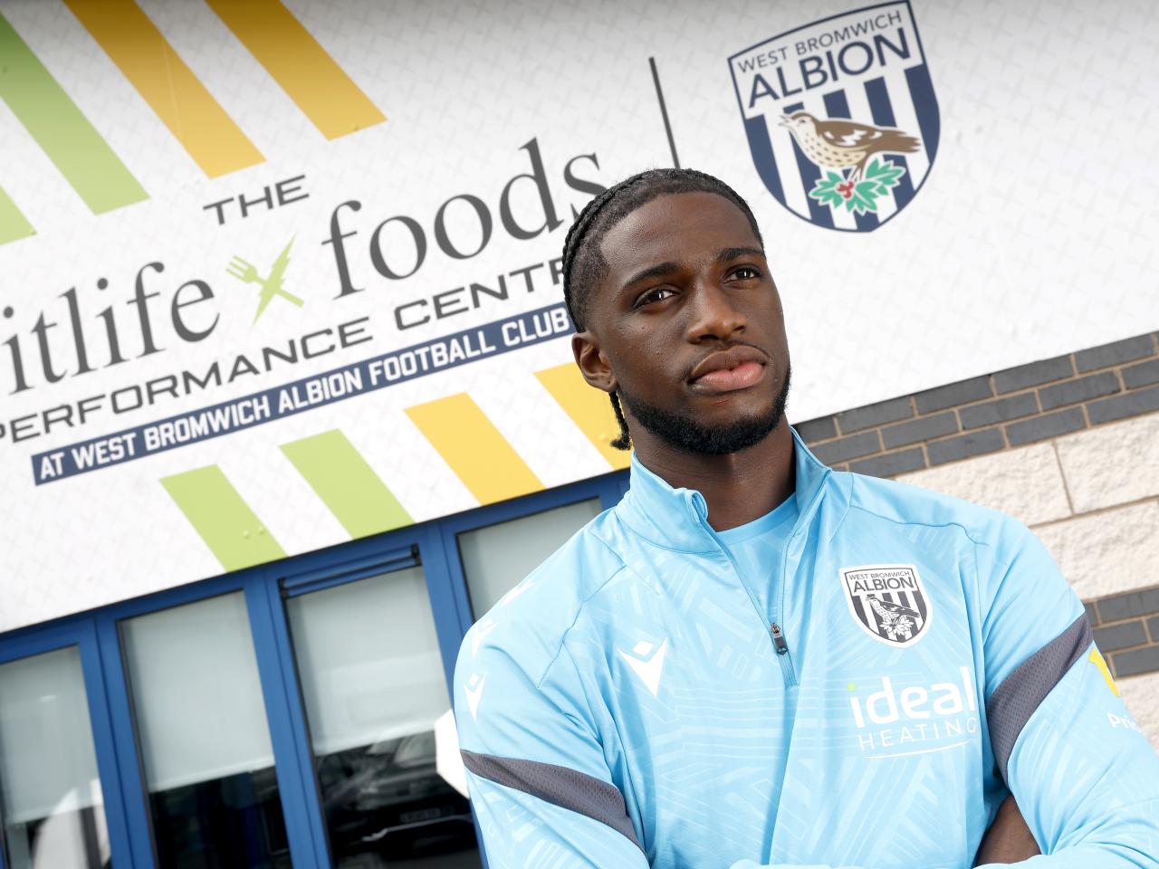 Samuel Iling-Junior looking at the camera while stood in front of branding outside the training ground