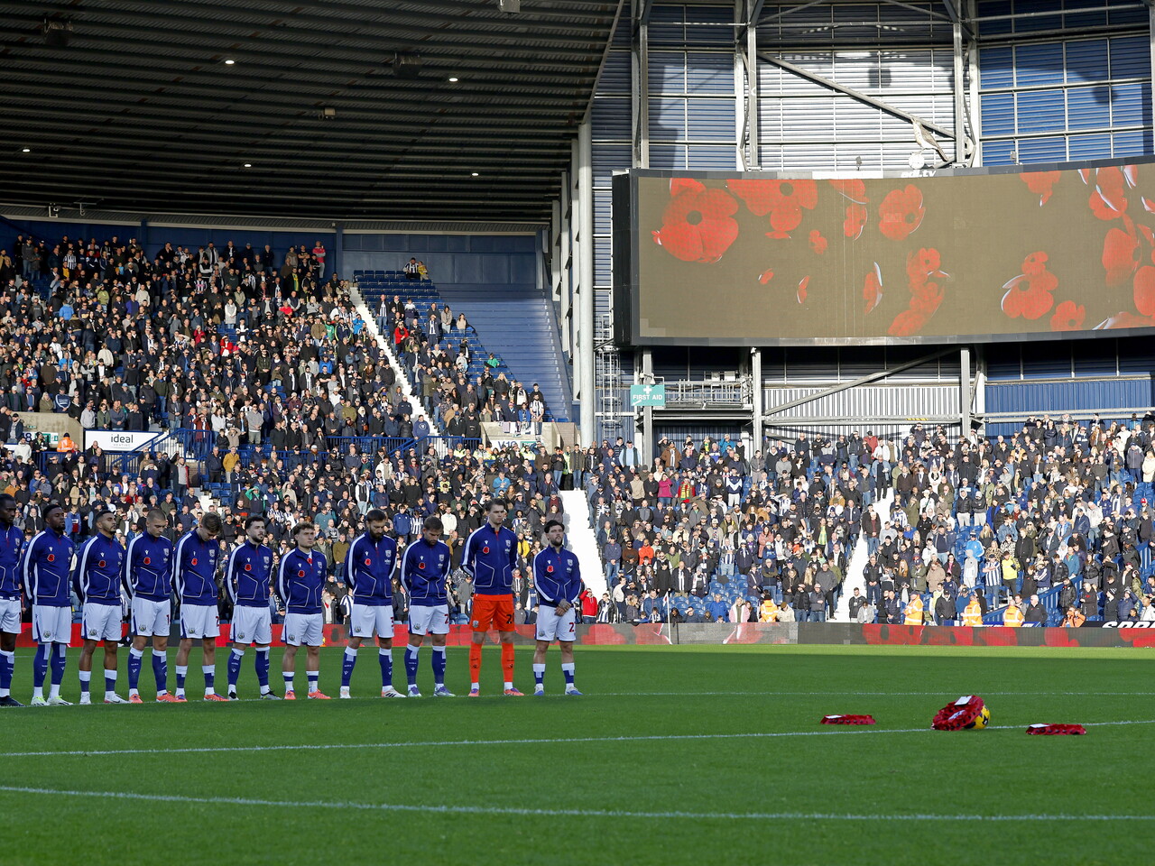 Albion players in a line on the centre circle during a silence with poppies on the big screen in the background 