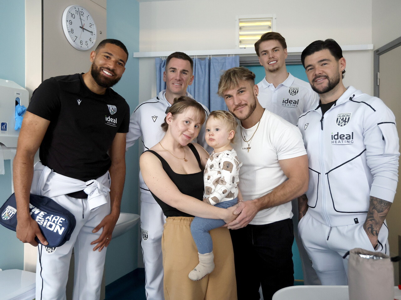 Four WBA players posing for a photo with a young family on a ward at the Midlands Met hospital