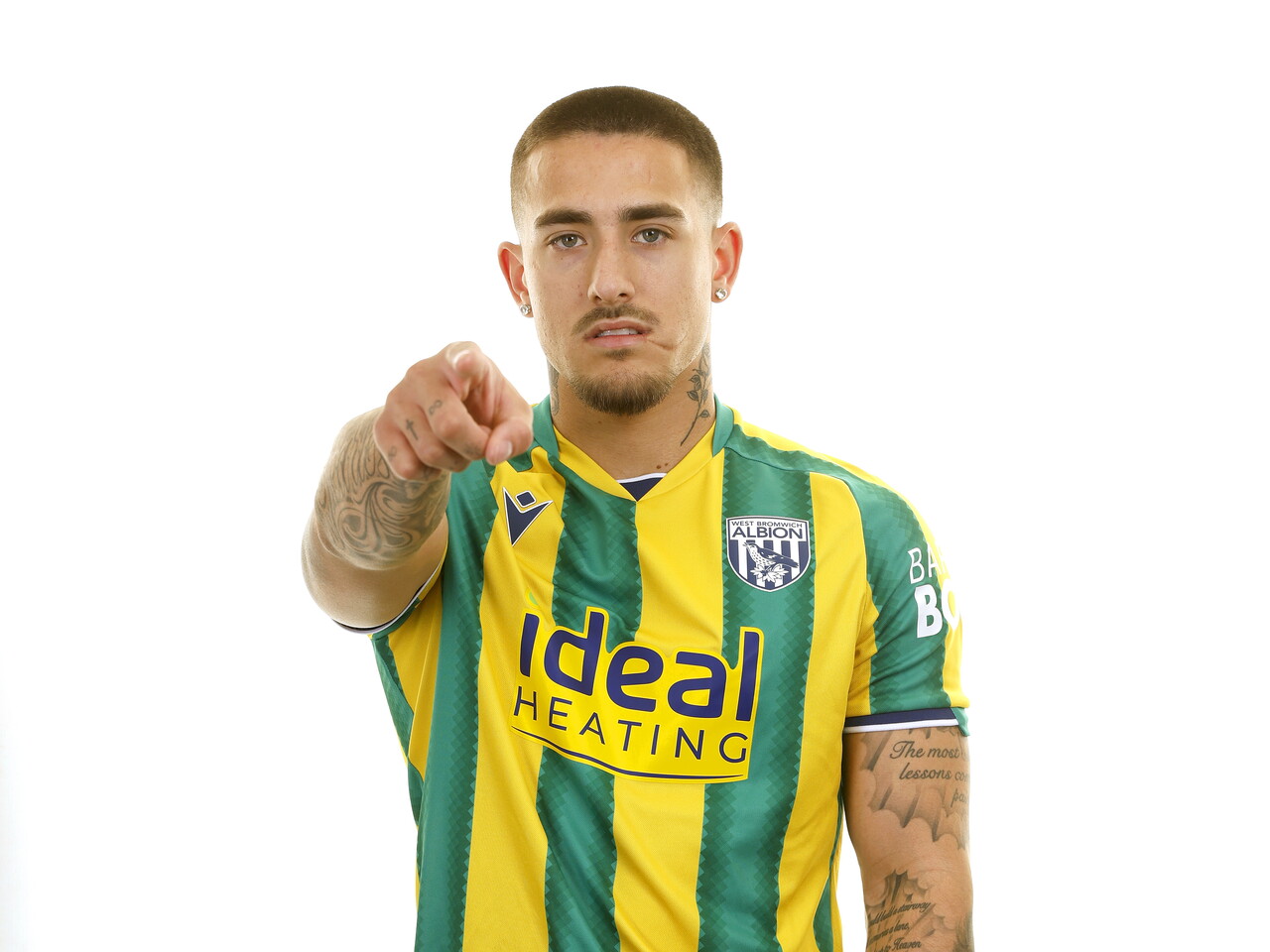 Danny Imray smiling and pointing at the camera while stood in front of a white background in a green and yellow away WBA shirt
