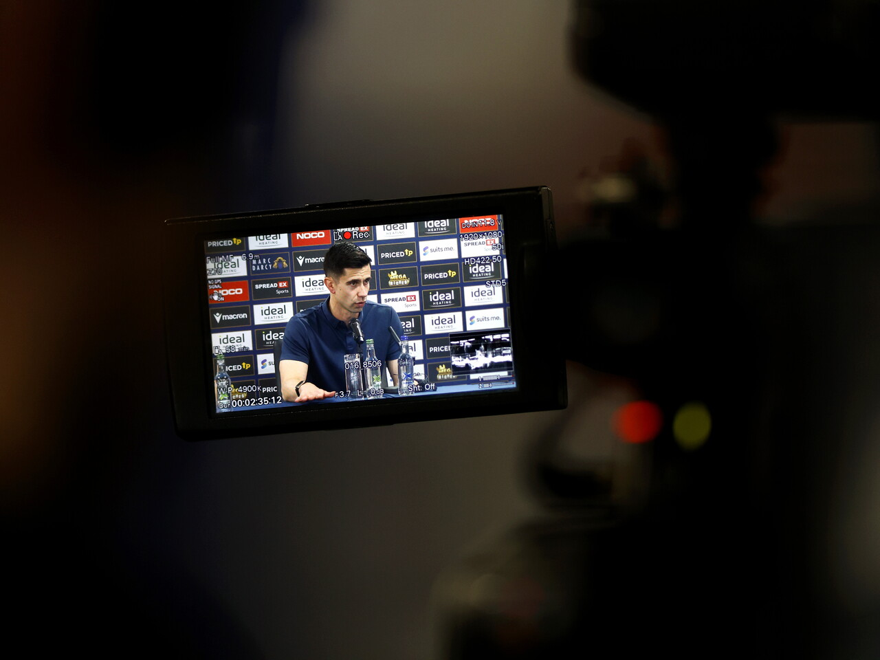 An image of Eric Ramsay at a press conference through a screen on a camera 
