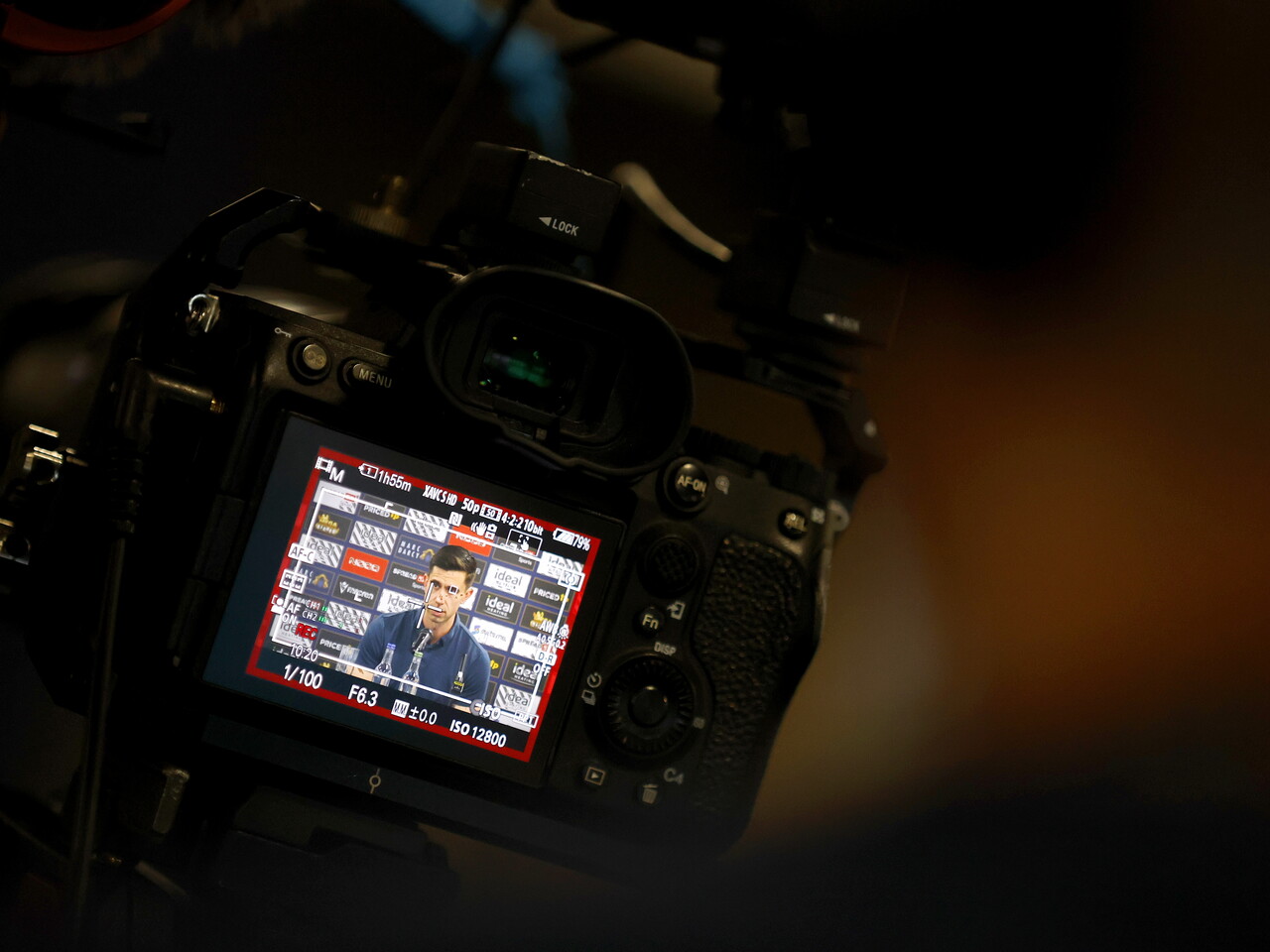 An image through a camera of Eric Ramsay in a press conference