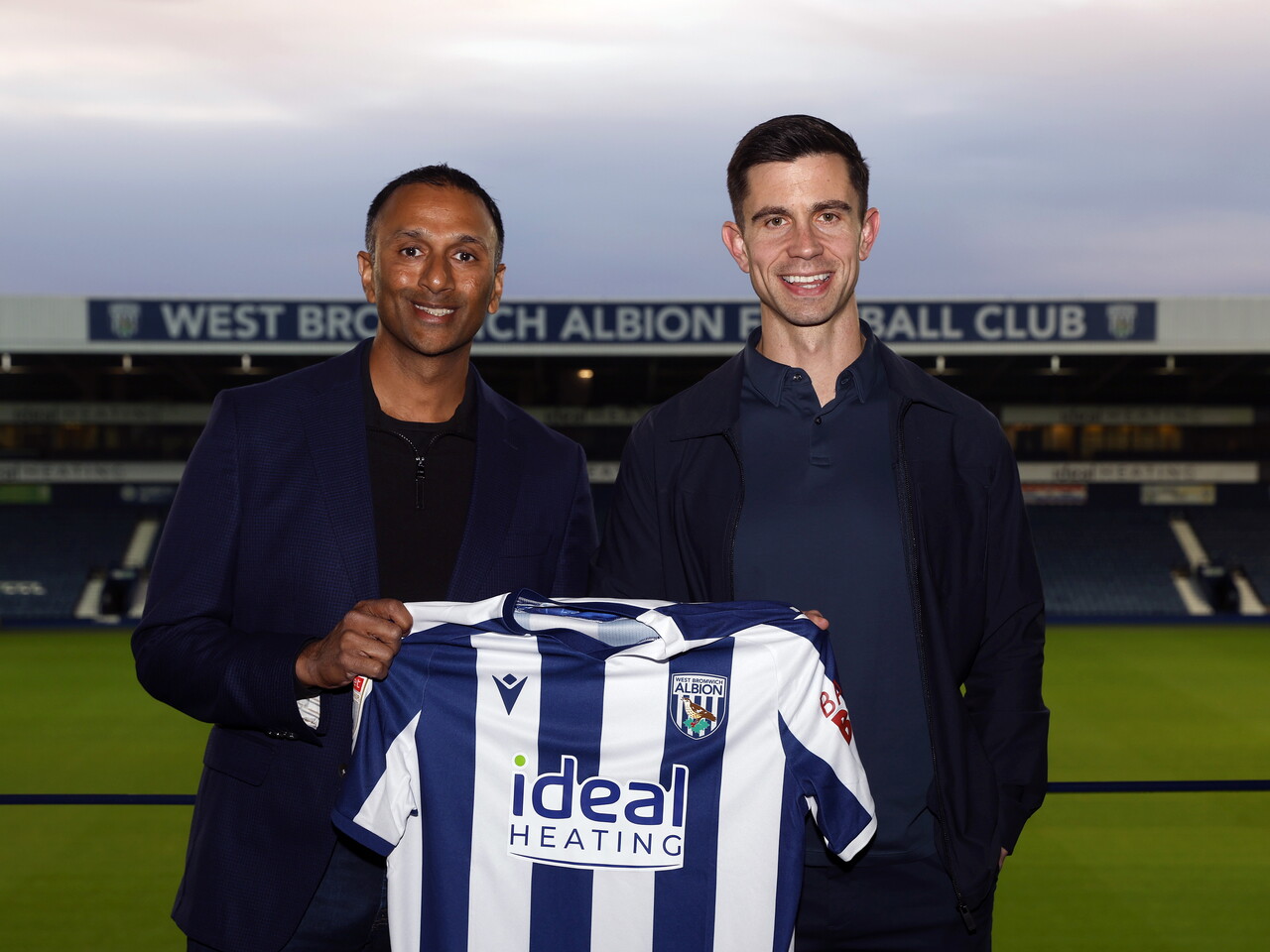 Eric Ramsay and Shilen Patel smiling at the camera and holding up a home WBA shirt at The Hawthorns