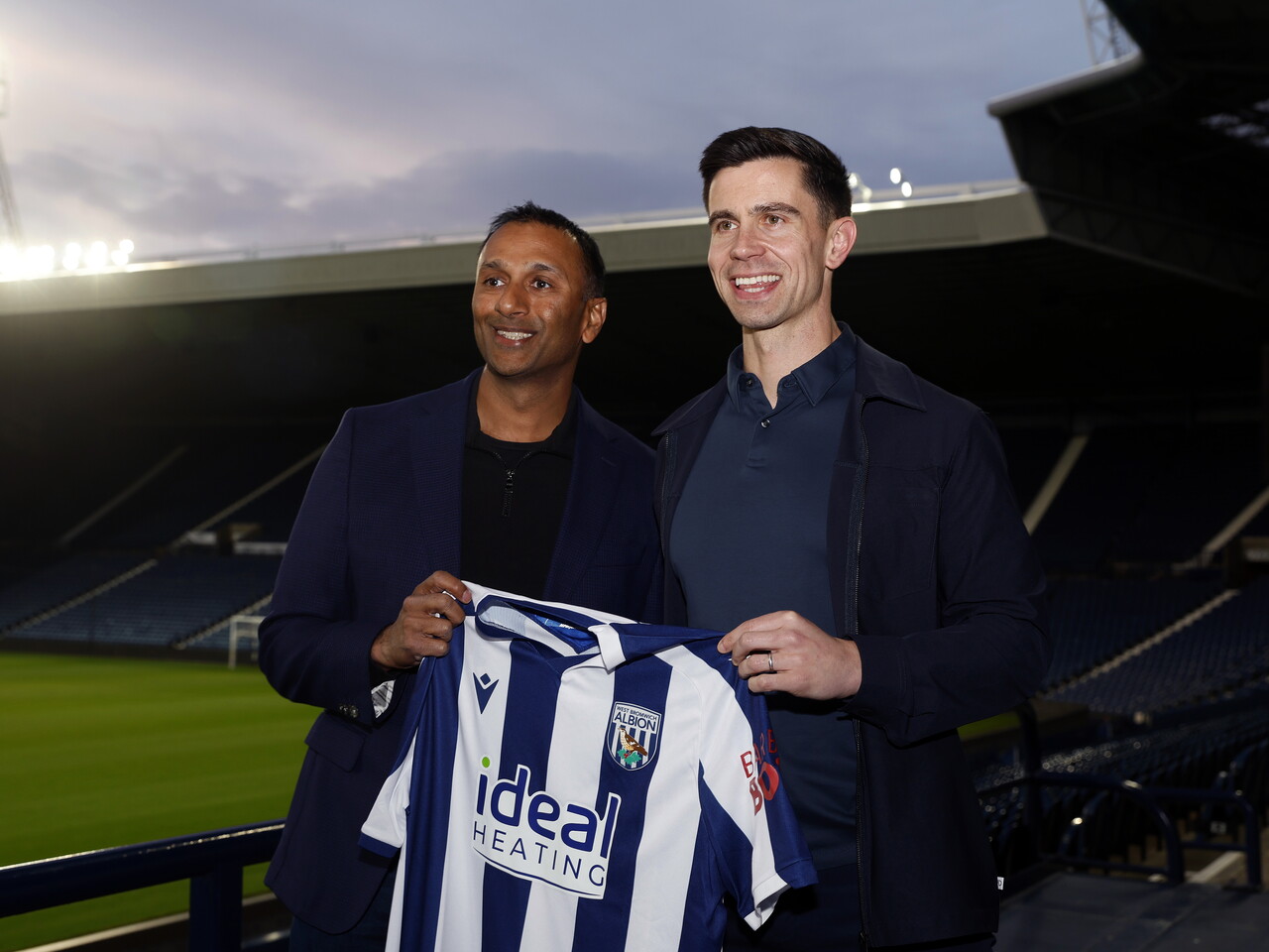 Eric Ramsay and Shilen Patel smiling at the camera and holding up a home WBA shirt at The Hawthorns