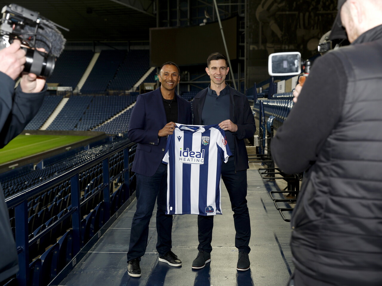 Eric Ramsay and Shilen Patel smiling at the camera and holding up a home WBA shirt at The Hawthorns