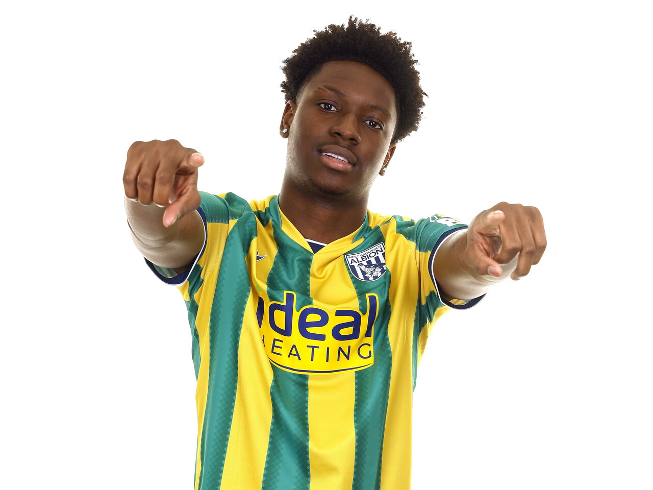 Jamaldeen Jimoh-Aloba smiling and pointing at the camera while in the green and yellow away kit in front of a white background