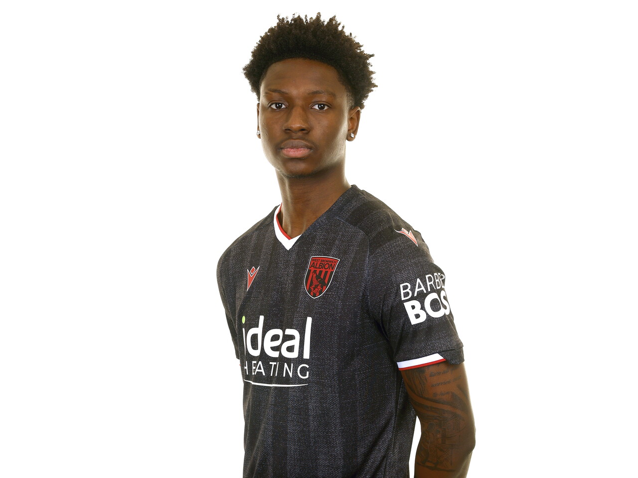 Jamaldeen Jimoh-Aloba smiling at the camera while stood in front of a white background in the black away kit