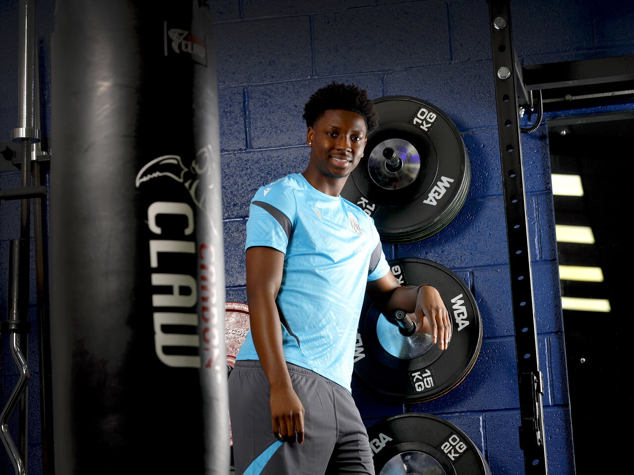 Jamaldeen Jimoh-Aloba smiling at the camera while leaning against equipment in the gym