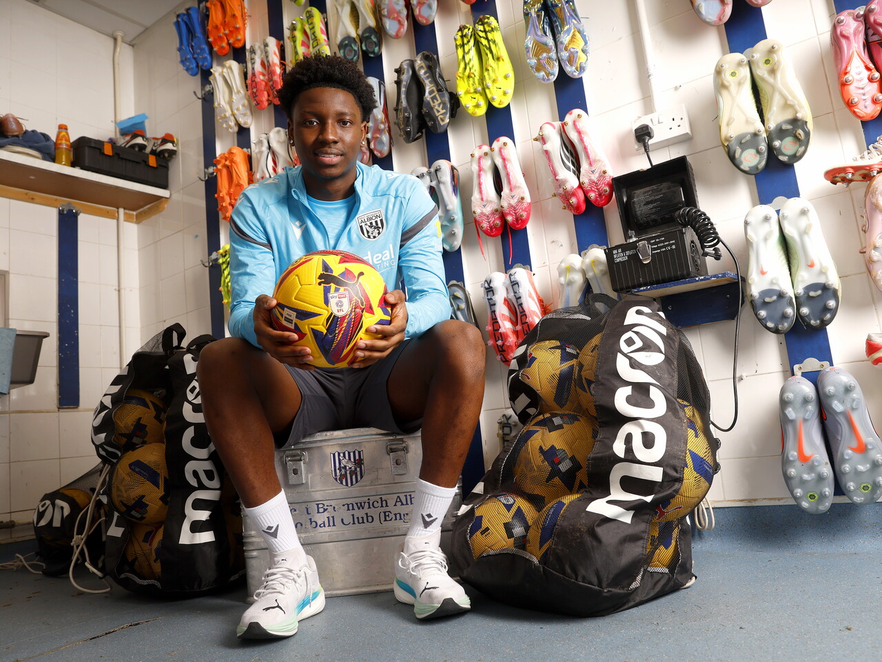 Jamaldeen Jimoh-Aloba smiling at the camera while sat in the boot room holding a ball