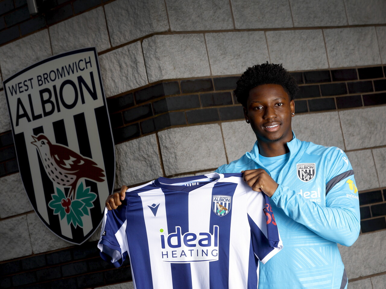 Jamaldeen Jimoh-Aloba smiling at the camera while holding up a home WBA shirt