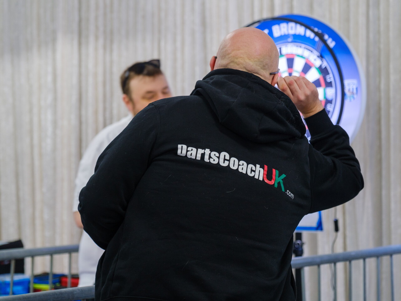 DartsCoach UK team member throwing a dart with branding on his hoodie