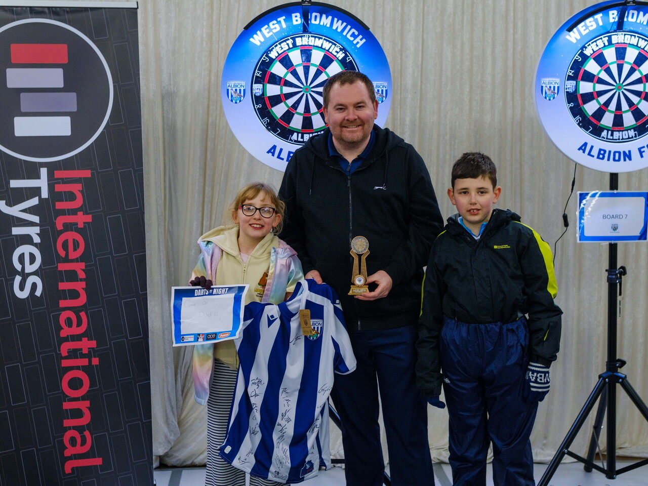 Adult winner Carl Sparrow holding trophy standing beside his children.