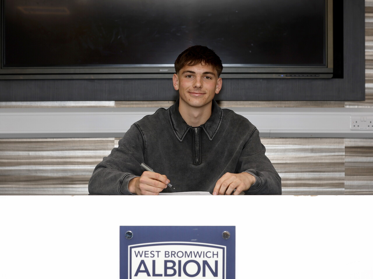 Charlie Blackshields smiling at the camera while signing a professional contract