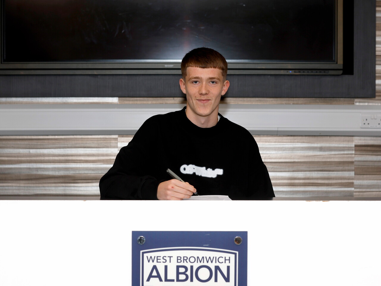 Ryan Colesby smiling at the camera while signing a professional contract