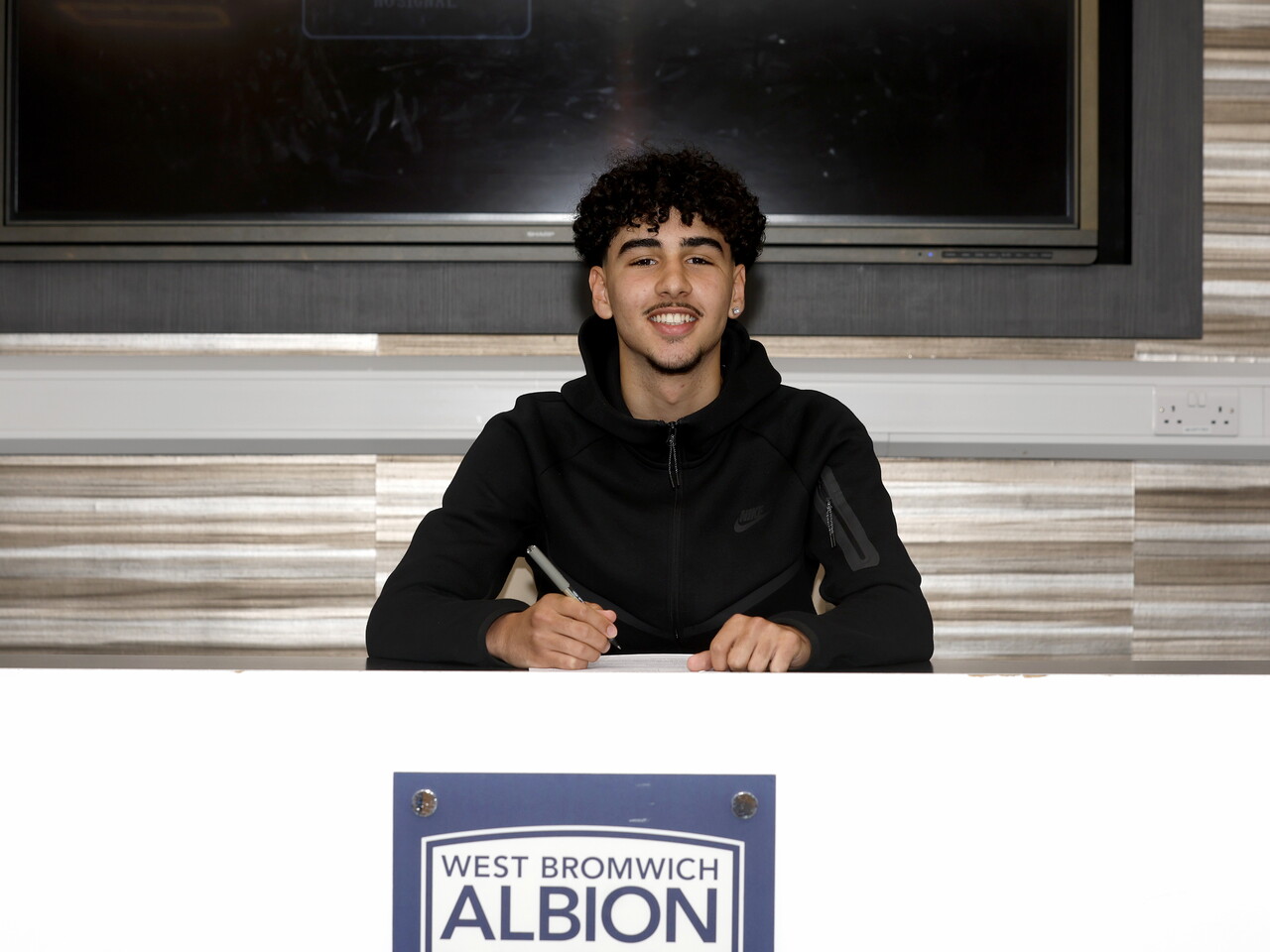 Adam Letlat smiling at the camera while signing a professional contract