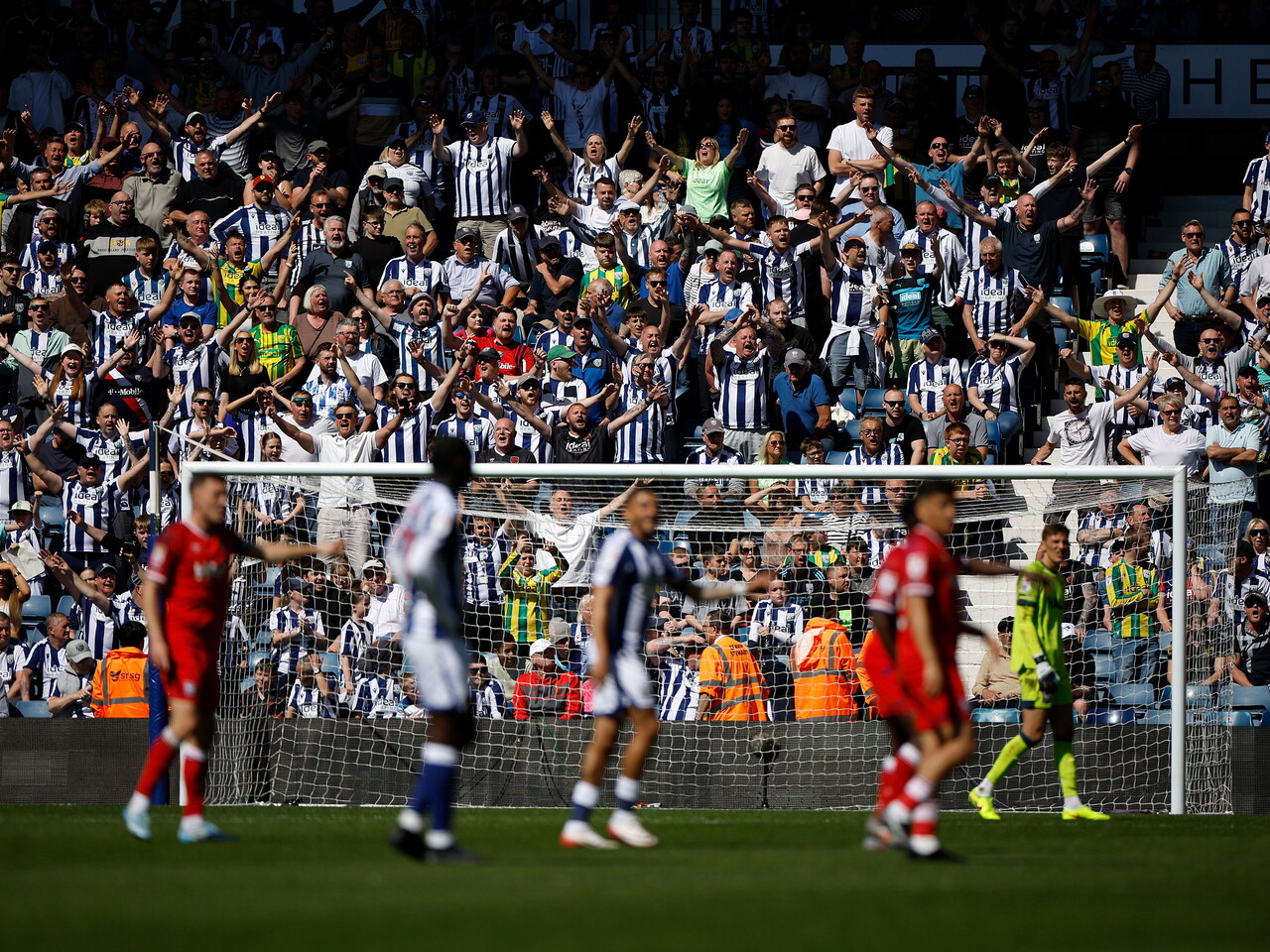 A view of WBA fans behind the goal cheering with action taking place on the pitch in front 