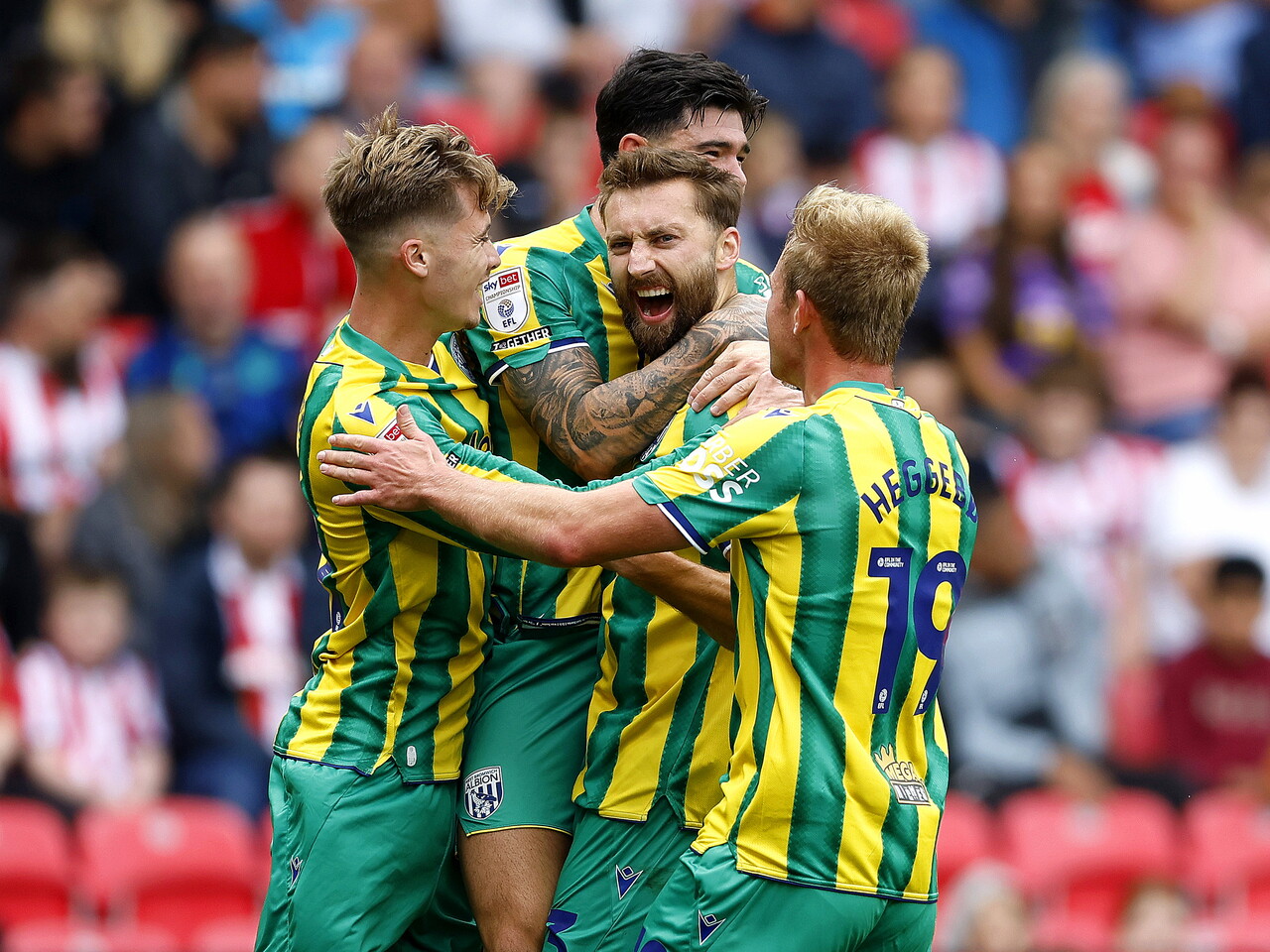 Several WBA players celebrating with Nat Phillips after his goal at Stoke City in the green and yellow away kit 