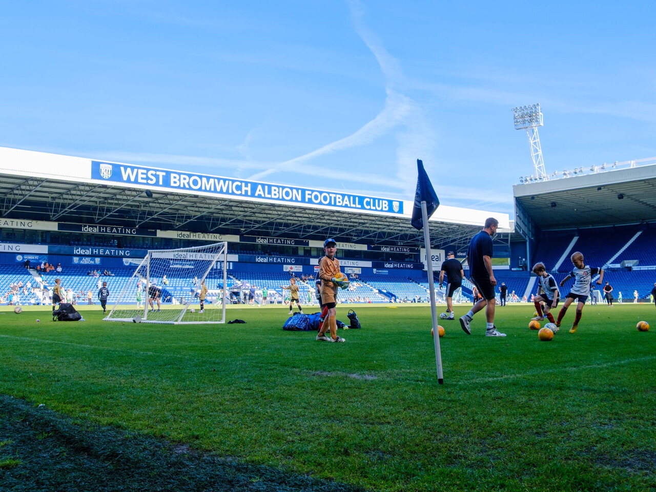 View of the pitch with players warming up and the West Stand in the background.