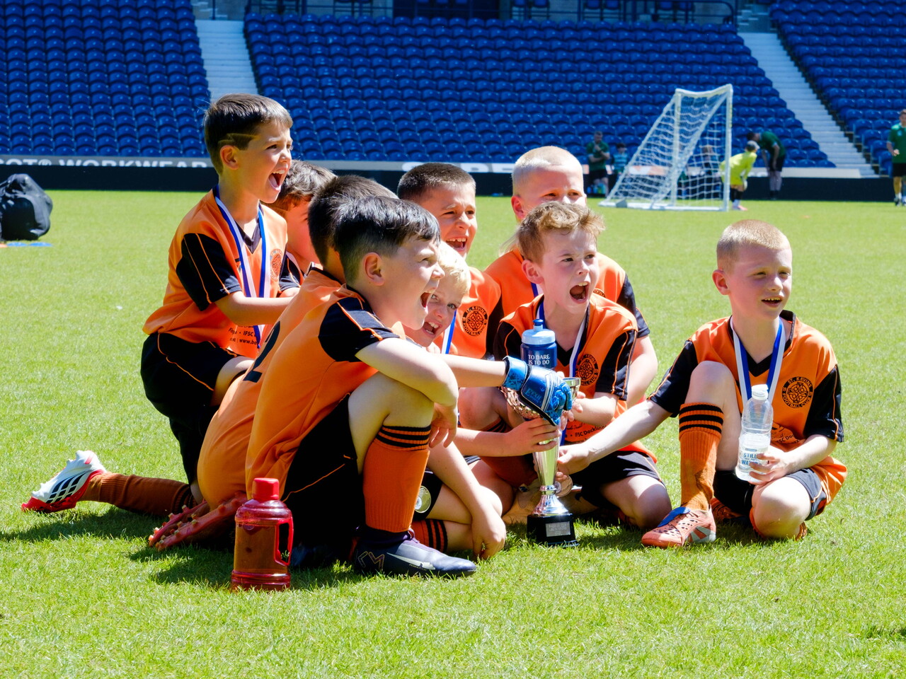 St Kevin's FC U8s seating on the pitch, cheering with the trophy
