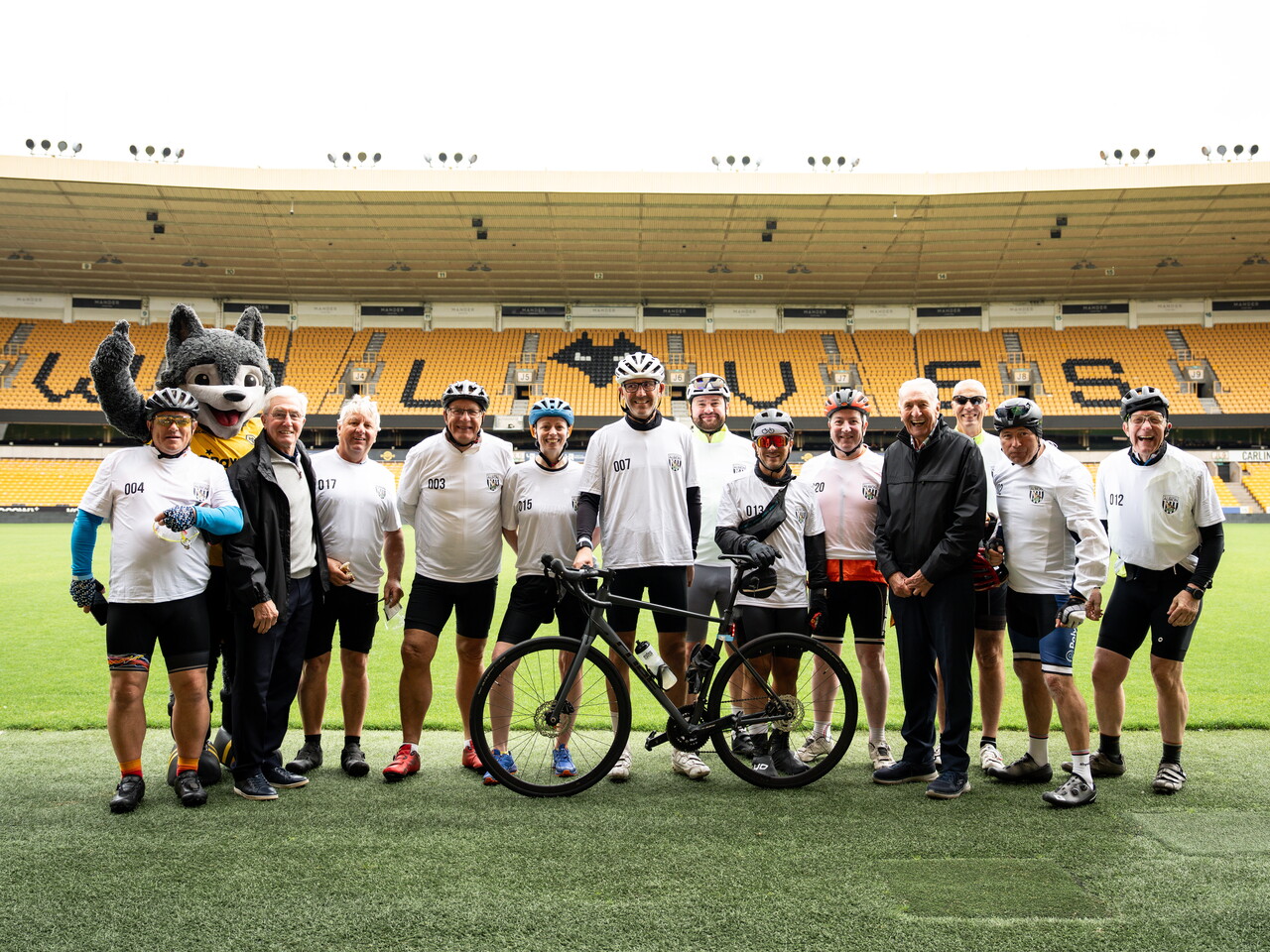 Albion cyclists pose with bicycles on the pitch inside Molineux Stadium