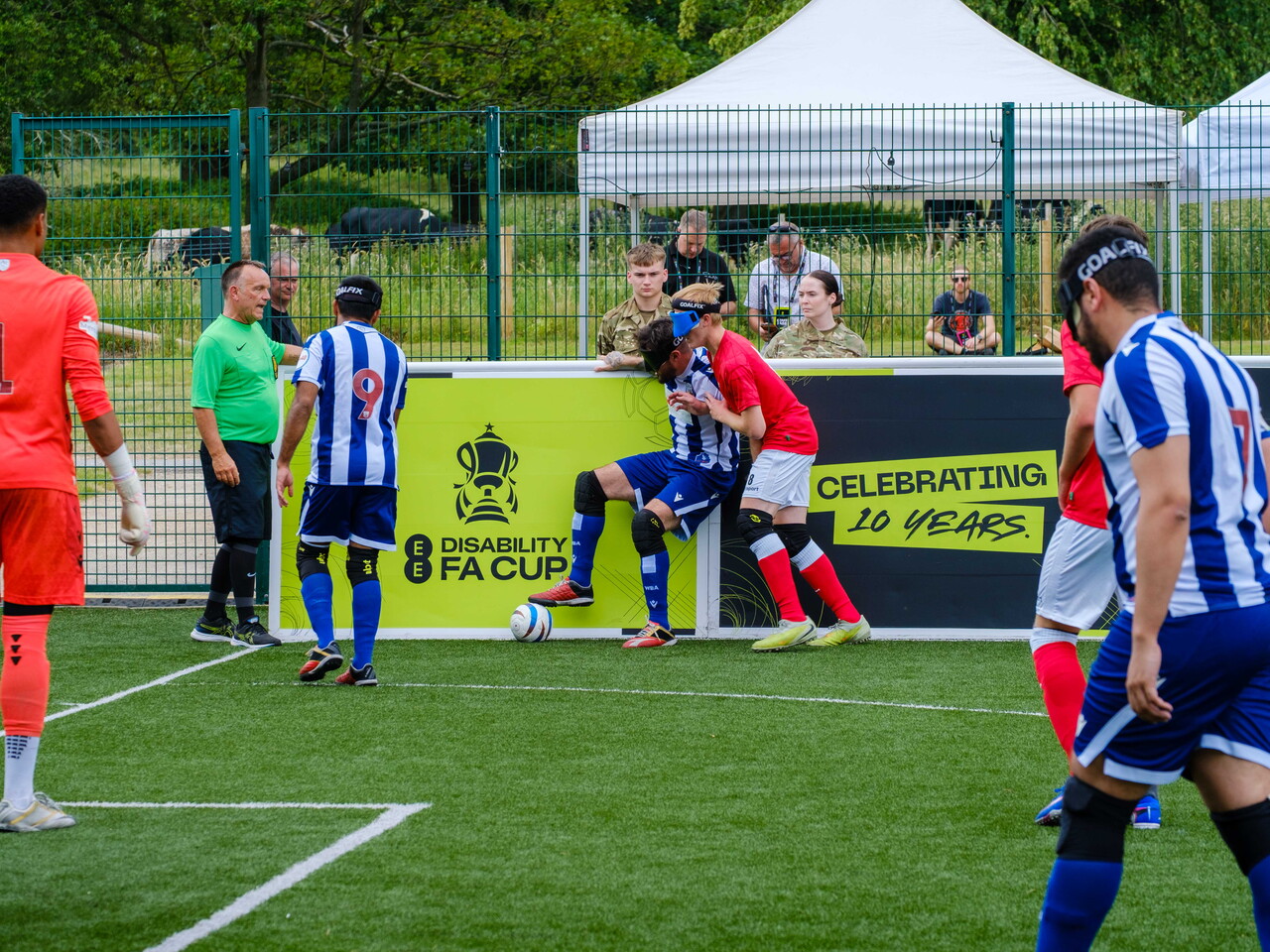 Eesa battling for the ball with a RNC player applying pressure. Players from both teams in the distance.