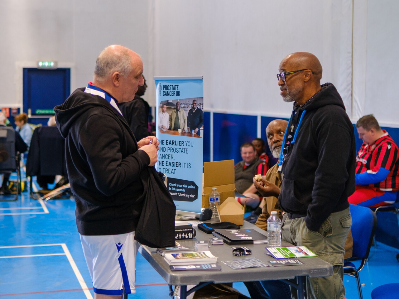 Cancer Kicker player in discussion with Prostate Cancer UK representative at the stall. 
