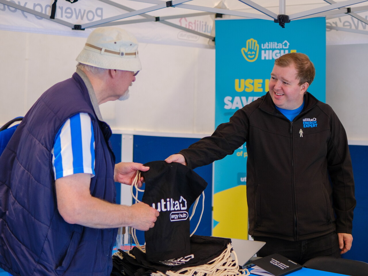 Utilita representative handing a drawstring bag to a participant at the stall. 