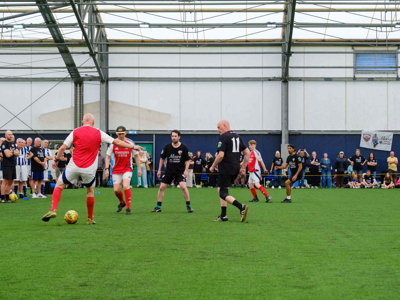 Wide shot of Moore than Cancer and Arsenal players in action with spectators on the sidelines.