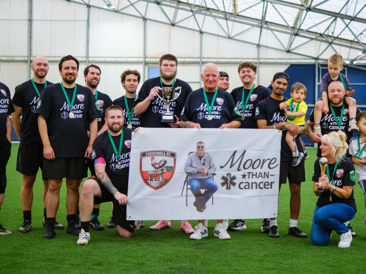 Moore than Cancer with trophy in front of tribute banner.