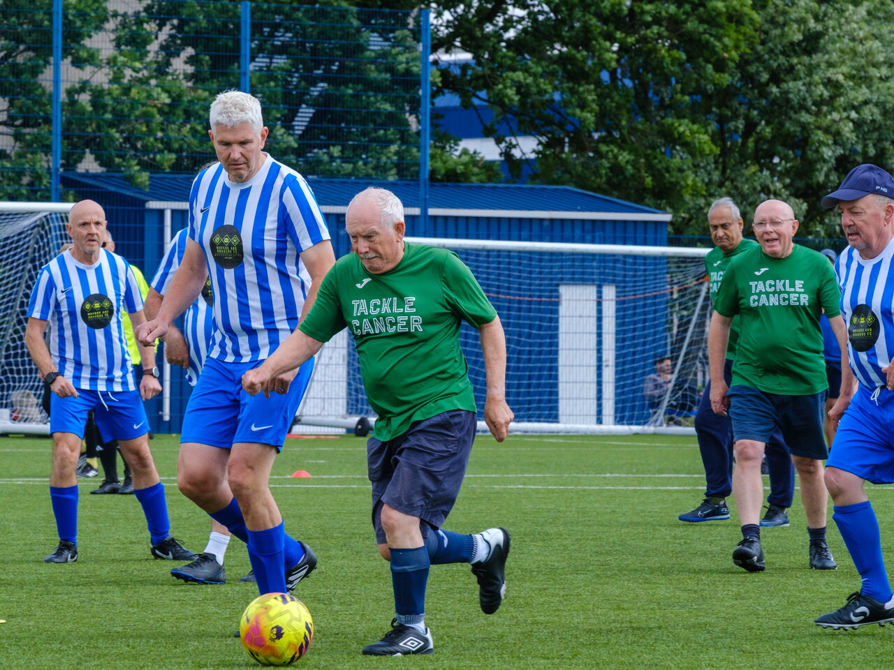 Wide shot of Big C tackling Cancer and Movers and Shakers on the pitch chasing the ball