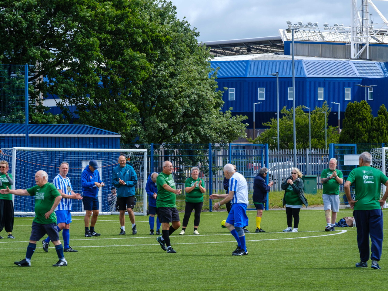 Wide shot of Big C tackling Cancer and Movers and Shakers shaking hands with The Hawthorns in the background.