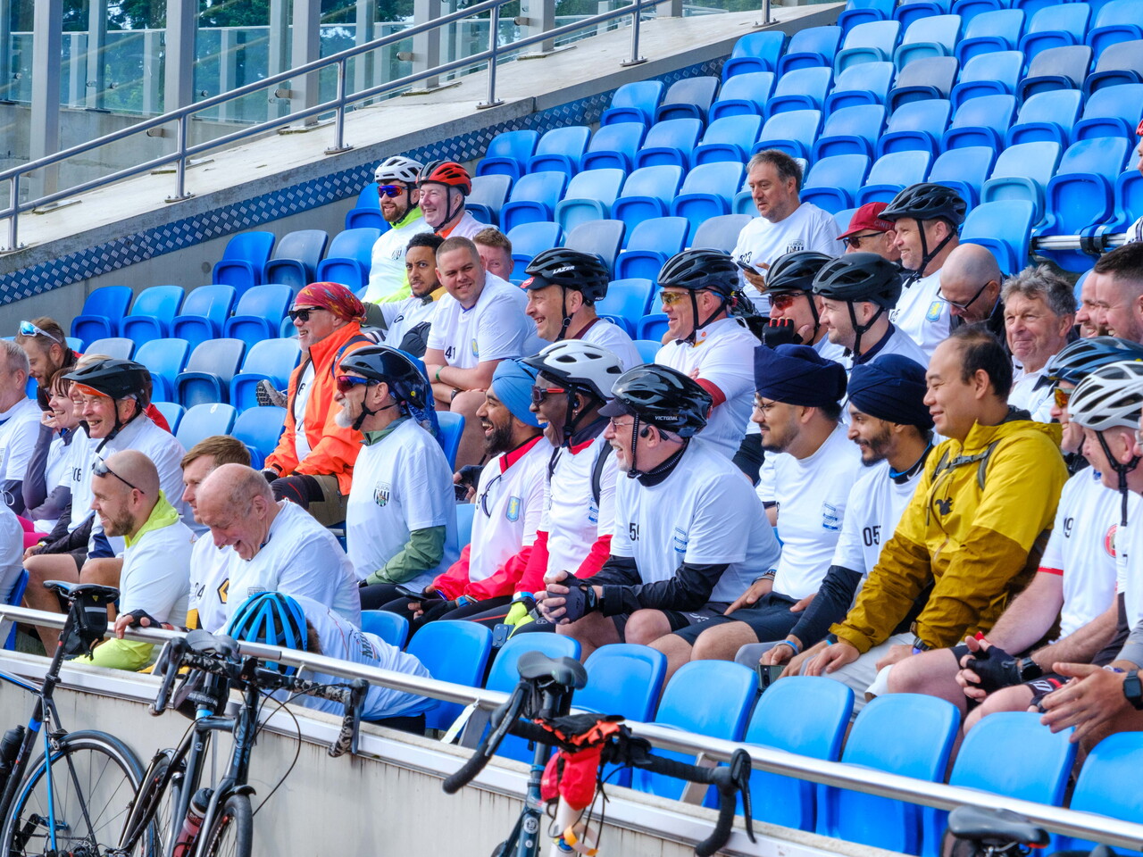 Participants in team jerseys seated together in stadium stands before the event.