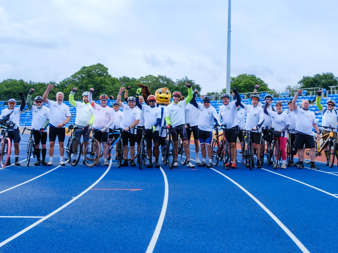 Cyclists pose with raised arms and bikes on the running track inside Alexander stadium.