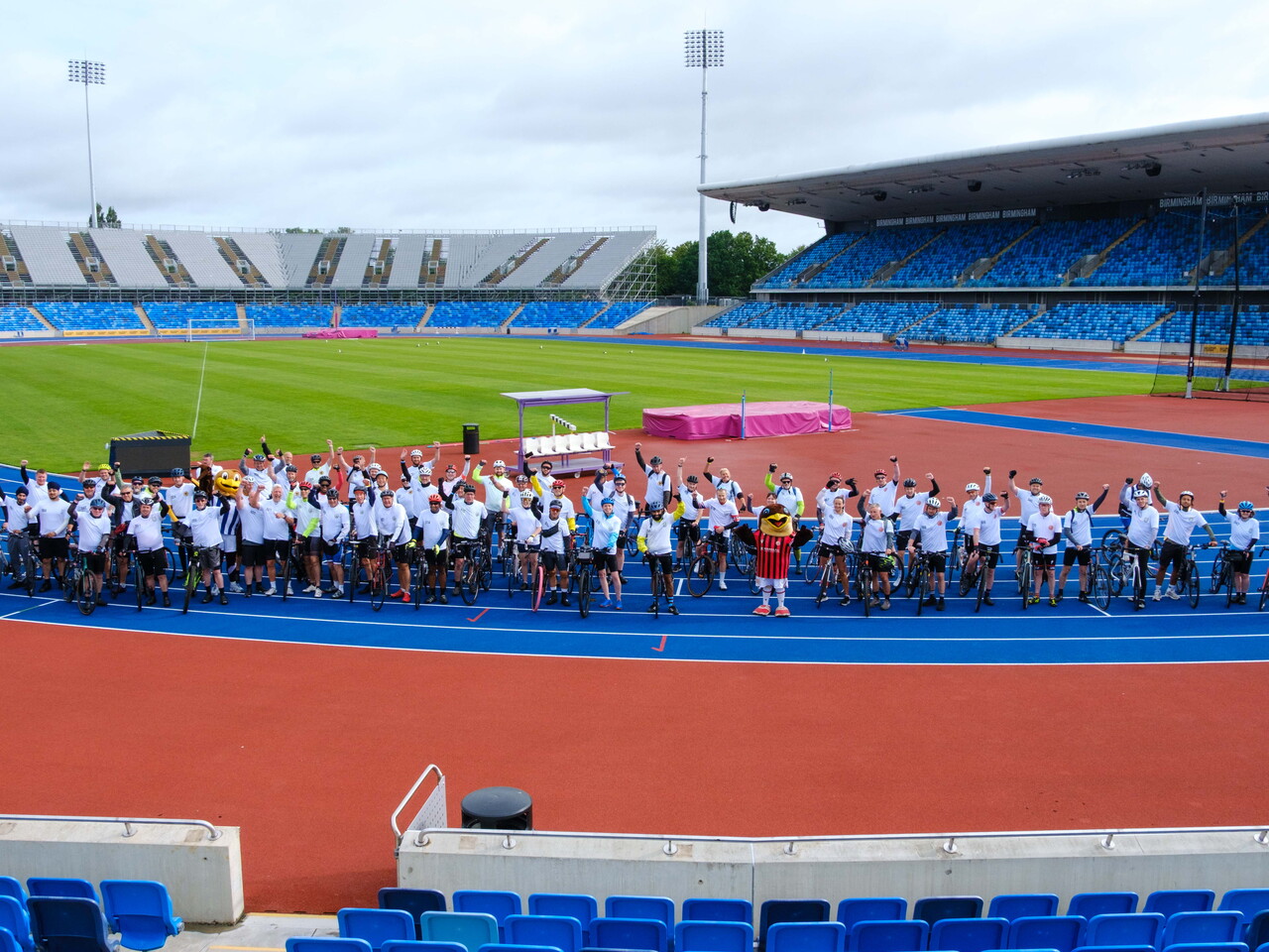  Large group of cyclists gathered on the track for a commemorative event photo.