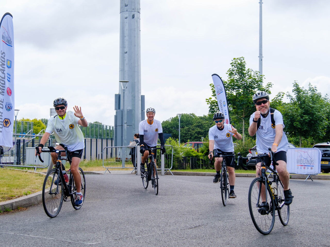 Riders smile and wave while cycling out of Alexander Stadium