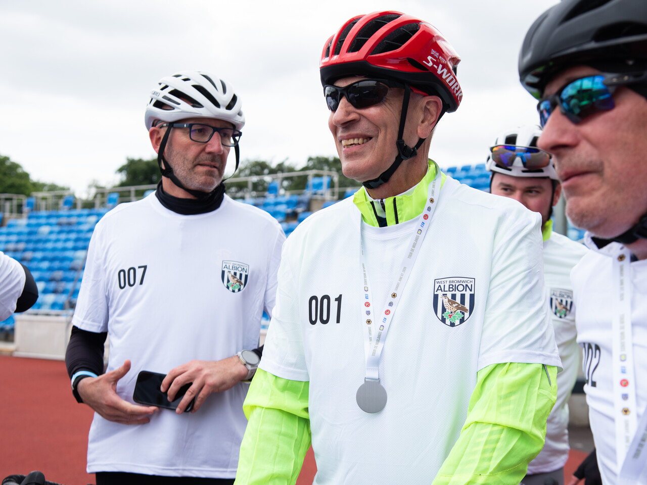 Medal-wearing cyclist smiles while speaking with fellow participants after the ride.