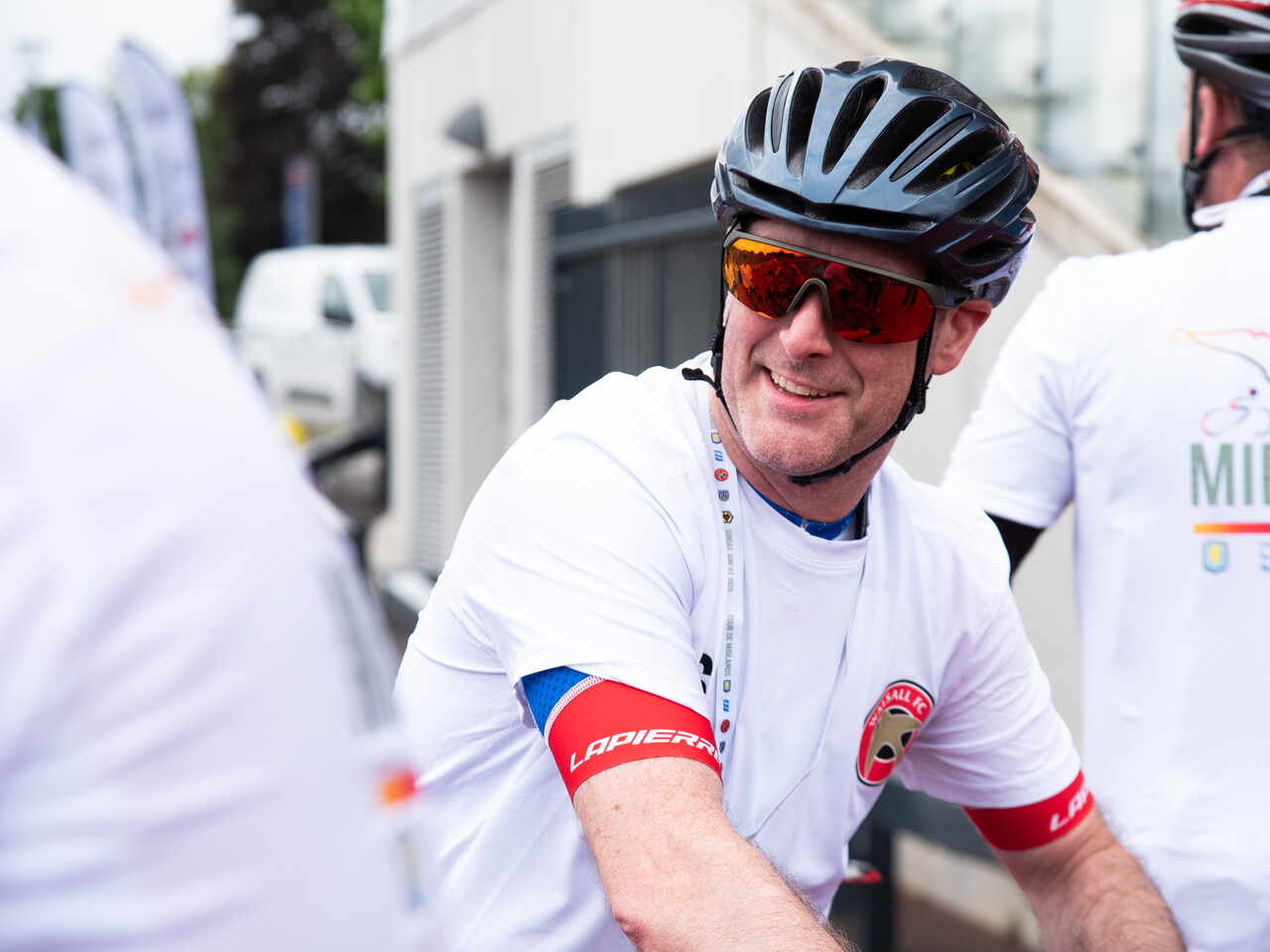 Cyclist wearing reflective sunglasses smiles while resting after the cycle.