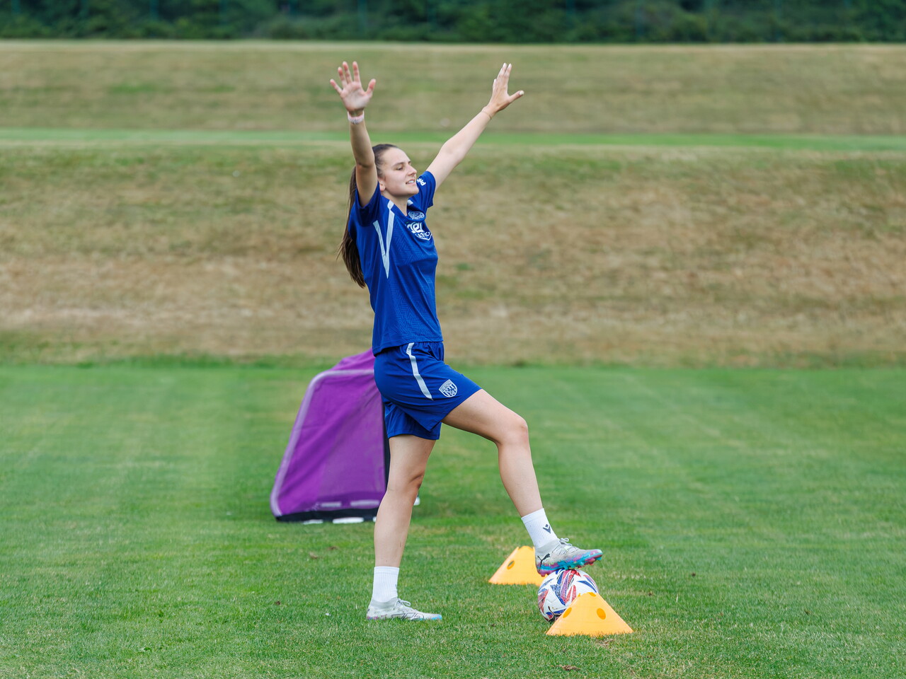 Izzy Green with her arms stretched up in the air and her foot on the ball during a training session