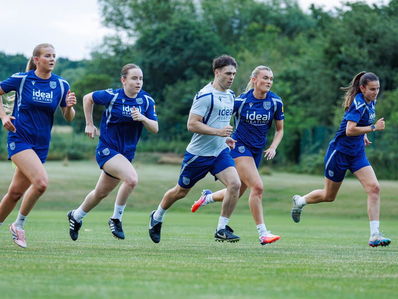 Four Albion Women players running in a line with a fitness coach during a training session