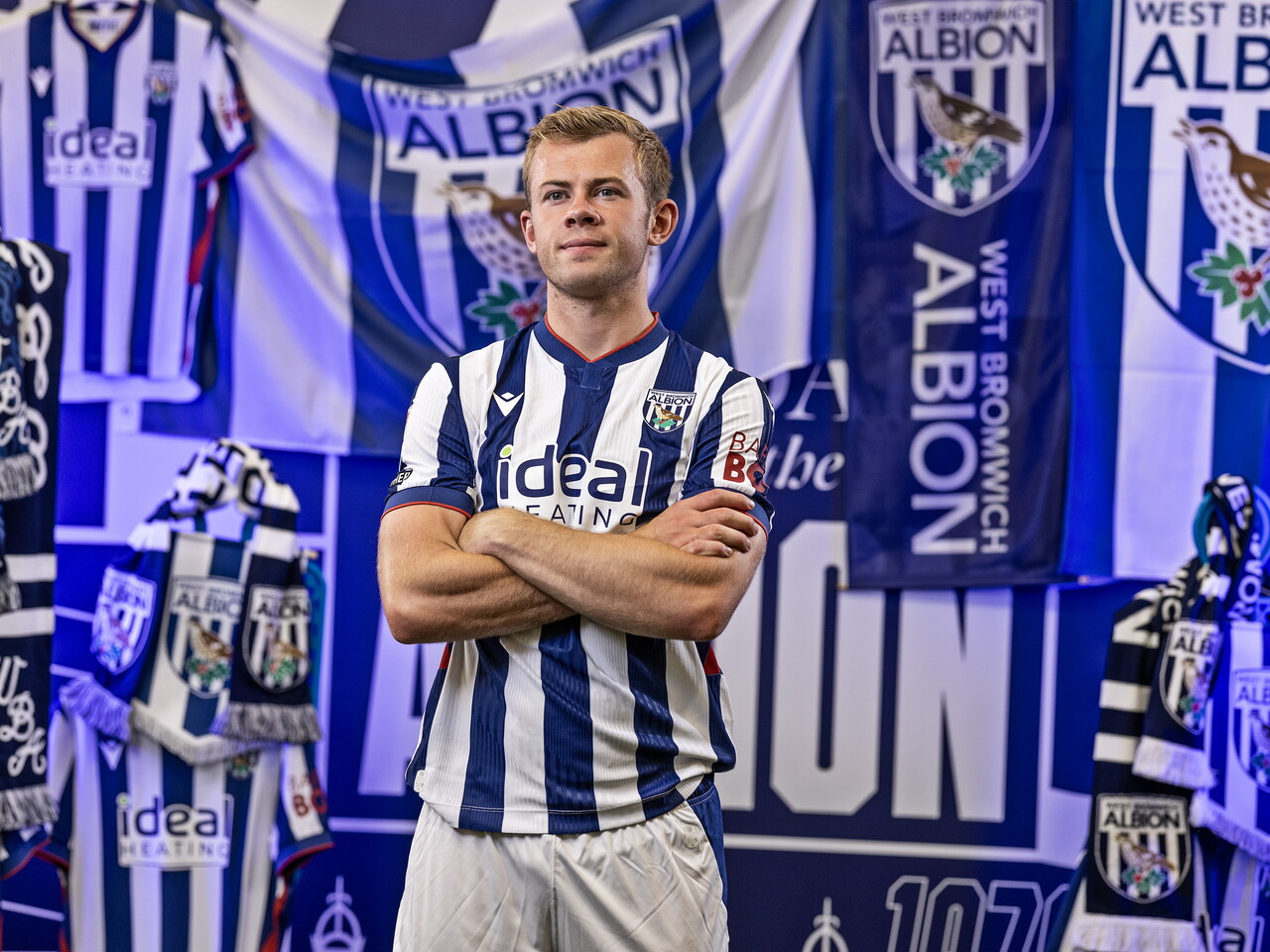 Aune Heggebø in the home kit looking at the camera with his arms folded while stood in front of an Albion back drop with plenty of WBA branding