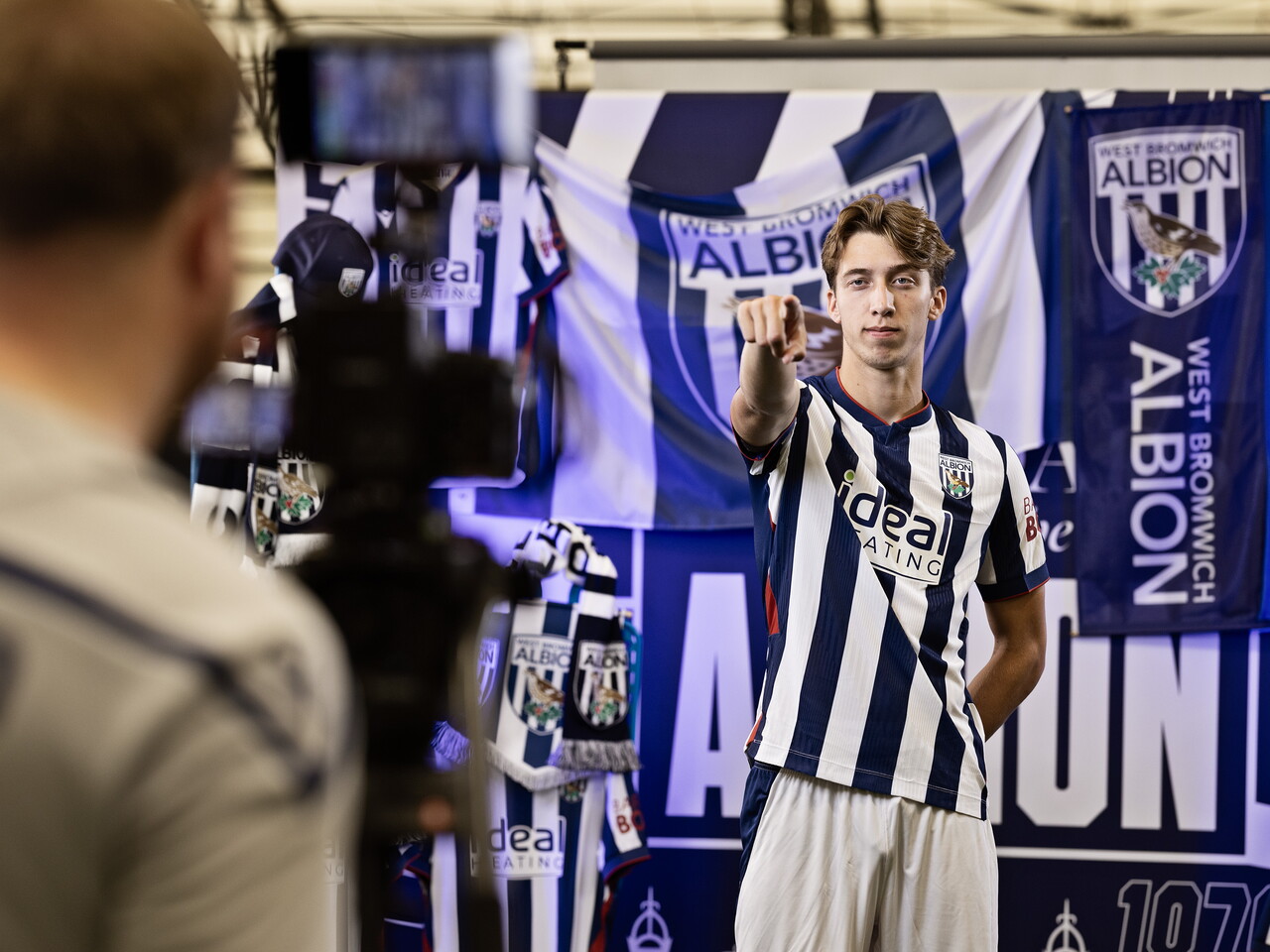 Harry Whitwell in the home kit pointing at the camera while stood in front of an Albion back drop with plenty of WBA branding
