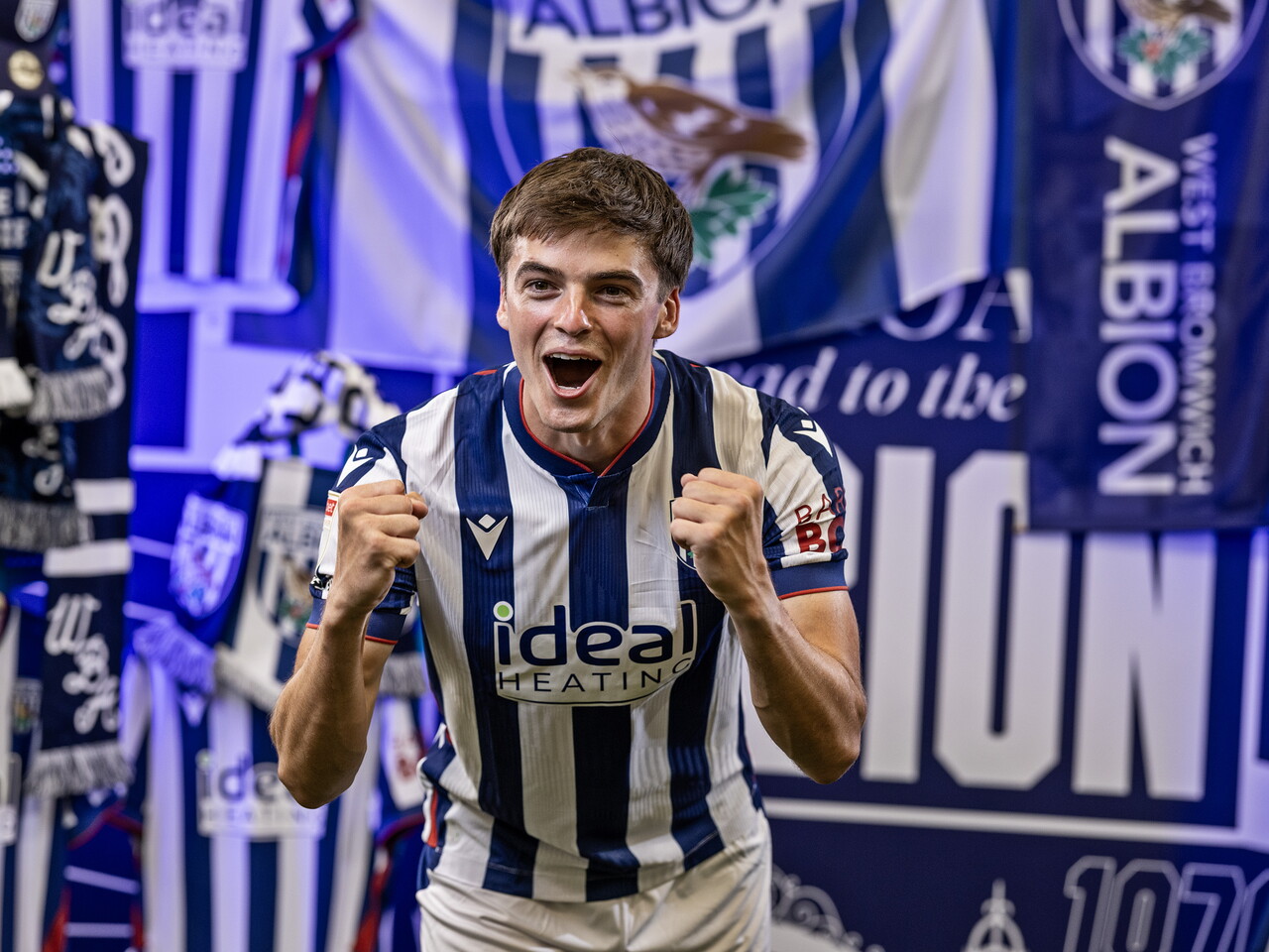 Alex Williams in the home kit celebrating towards the camera while stood in front of an Albion back drop with plenty of WBA branding