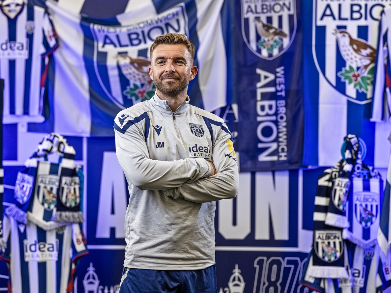 James Morrison smiling at the camera with his arms folded while stood in front of an Albion back drop with plenty of WBA branding